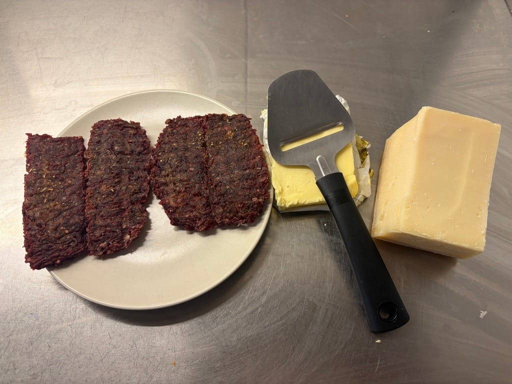 Dried meat on a plate next to butter, Parmesan and a cheese slicer